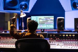 Sound engineer counting down to record singer in sound booth, doing a sign to let the artist know when to start the performance. Audio technician operating control room panel board desk. photo