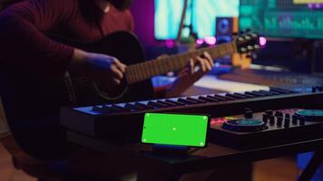 Songwriter playing acoustic guitar in home studio with greenscreen display running on smartphone app. Musician practices singing on musical instrument with strings, isolated screen. Camera A. photo
