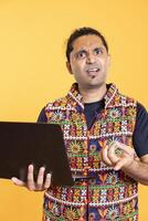 Portrait of IT employee frowning after seeing virus error message on laptop screen while doing job tasks, studio background. Software developer feeling puzzled, confused by technology bugs on notebook photo