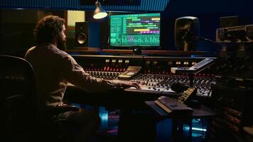 Sound designer recording tunes to create a new song in control room, working on his new album with mixing console and faders. Audio technician producing tracks, pushing sliders. Camera B. photo