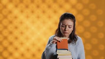 Portrait of woman browsing through stack of textbooks, gathering information for school exam, isolated over studio background. Person searching necessary course for exam in pile of books, camera A photo