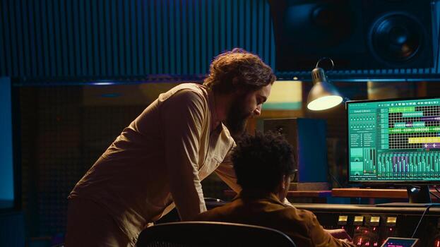 Diverse team of musician and audio technician creating a hit song, working in professional music studio. Artist with producer editing and recording tracks on mixing console panel. Camera A. photo