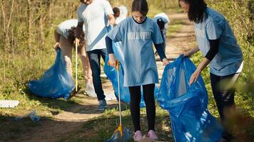 Mother and daughter cleaning up the woods with proper tools and trash bags, grabbing and recycling garbage to save the planet. Activists team collecting rubbish to stop forest pollution. Camera A. photo