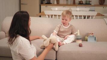 Happy family at home. Mother and baby boy playing with toys in couch at home indoors. Little toddler child and babysitter nanny having fun together. Young woman mom kid son rest in living room video