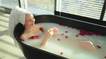 Spa relaxation. Woman lying in bath with red roses petals. Girl relaxing in bathroom at home. Pretty female enjoying taking hot bath. Stress relief. Rest after hard working day video