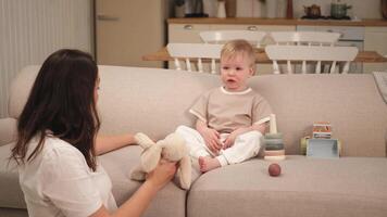 Happy family at home. Mother and baby boy playing with toys in couch at home indoors. Little toddler child and babysitter nanny having fun together. Young woman mom kid son rest in living room video