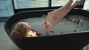 Spa relaxation. Woman lying in bath with holding glass with red wine. Girl relaxing in bathroom at home. Pretty female taking hot bath drinking wine. Stress relief. Rest after hard working day video