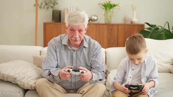 Happy family. Old senior man grandfather boy grandson playing game with joysticks at home. Smiling grandparent and child using gamepads for game. Older generation modern tech usage video