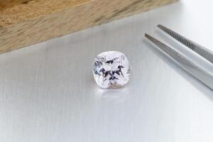macro mineral faceted stone Morganite with tweezers on a gray background photo