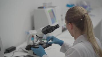 Female medic in uniform working with microscope making analysis at laboratory office. Scientist working in laboratory. Microbiologist woman working in modern medical lab with technological equipment. video