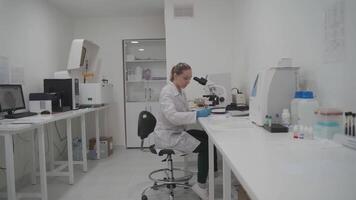Female medic in uniform working with microscope making analysis at laboratory office. Scientist working in laboratory. Microbiologist woman working in modern medical lab with technological equipment. video