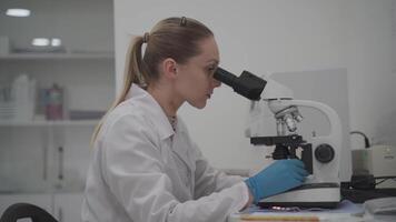 Female medic in uniform working with microscope making analysis at laboratory office. Scientist working in laboratory. Microbiologist woman working in modern medical lab with technological equipment. video