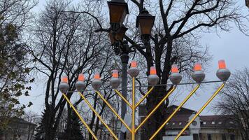 Hanukkah lights glow against the backdrop of a winter city of bare trees and sky lanterns close up of Hanukkah Doughnuts being sprinkled with powdered sugar in slow motion video