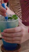 Blue drink with mint cool drink with mint and ice in a glass with a blue straw on a lawn. rotating glass with lime lemonade and mint leaves and splashes from a falling ice cube video