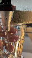 Take a glass of cold water. filled glass of water is on the table in the kitchen. In the background there is a faucet and a filter for water purification. A man takes a glass of water from the table video
