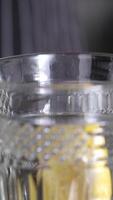 Close of lemon slice in female hand dropping in water and ice cubes in blue glass. Round lemon piece in beverage in slow motion macro view. video