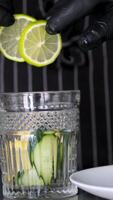 Add lemon to glass. Making lemonade, summer drink, cold drink, healthy liquid. Throw a slice of lemon into a glass Citrus fall water dropped glass closeup. Cold water with ice cubes and lemon slice video