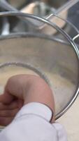 add flour through a sieve into the dough Extreme close up of woman s hand sifting flour through a small sieve adding it with a spoon. Handheld real time close up shot video
