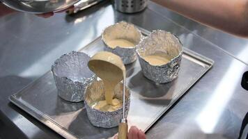 Woman pouring dough into a mold. Make a chocolate cake at home. ladle pour batter into homemade foil molds bake Easter small cake bento cake. pour the dough into the mold video