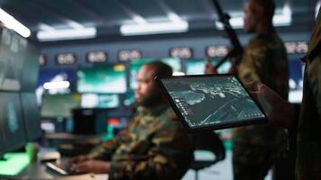militär ombud arbetssätt i kontrollera rum, använder sig av programvara på läsplatta, analyserar antenn spaning data. stänga upp av intelligens kår expert- kontrollerande drönare med bärbar enhet, kamera b video