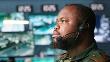 Military dispatcher relays info from army intelligence analysts to troops on front lines, close up shot. Radio communications operator wearing uniform talking in headset mic, camera A video