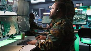 Military dispatcher relays info from army intelligence analysts to troops on front lines, close up shot. Radio communications operator wearing uniform talking in headset mic, camera B video