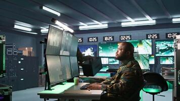 Military agent working in control room, analyzing aerial reconnaissance data and talking with colleague. Intelligence corps agent checking screens, discussing with coworker, camera B video