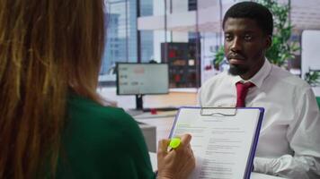 HR staff and applicant discussing the employment contract terms during the interview, providing explanations and clarifications. Job candidate reading the work agreement in high end office. Camera B. video