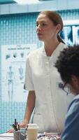 Vertical Specialist leading a department meeting with medical team to discuss treatment service, analyzing test results with staff to improve collective work. Using health care records for help. Camera B. video