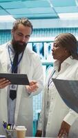 Vertikale Arzt und Krankenschwestern Überprüfung medizinisch Diagramme und Prüfung Ergebnisse, Zielen zu liefern das Beste Pflege im ein Krankenhaus Umfeld. vielfältig Mediziner Beratung Gesundheitswesen Aufzeichnungen zum Kontrolle. Kamera b. video