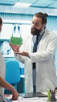 Vertical Medic presenting a box with isolated mockup screen during a meeting for disease prevention, conducting analytics and control of x ray scans results in a facility. Radiology department. Camera B. video
