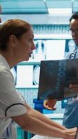 Vertical Physicians and radiologists analyzing x ray scans to create an effective treatment plan. Medics doing teamwork at a private clinic to ensure radiography based diagnostics for healthcare. Camera B. video