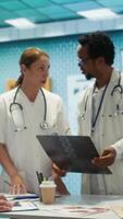 Vertical Specialists discuss x ray results and patient care strategy in a medical office. Team of licensed doctors working together to provide accurate diagnosis and effective treatment plans. Camera B. video