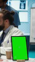 Vertical Team of doctors consulting analytics next to green screen on laptop in medical cabinet, examining x ray results to find the diagnosis. Licensed medics review hospital records at desk. Camera B. video