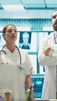 Vertical Team of medical specialists examining diagnostic data and hospital records, using a holographic image in cabinet. Experts looking into treatment plans on hologram at clinic. Camera A. video