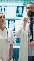 Vertical Doctor specialists reviewing human anatomy scans via hologram projection in cabinet, ensuring effective treatment plans. Team of healthcare experts use augmented visualization. Camera A. video