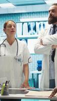 Vertical Team of medical specialists examining diagnostic data and hospital records, using a holographic image in cabinet. Experts looking into treatment plans on hologram at clinic. Camera B. video