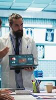 Vertical Professional medic analyzing mri brain scan with his staff in medical office, neuroscientist examining tomography with diverse doctors. Experts in neuroscience at treatment center. Camera B. video