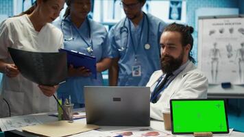 Diverse team of medics analyze x rays next to mockup copy space and discuss treatment plans in a medical office. Healthcare specialists working to provide diagnosis on insurance. Camera B. video