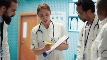 General practitioner highlighting important test results on hospital records, working with his staff in a treatment center. Medic specialist examining diagnosis for disease prevention. Camera A. video