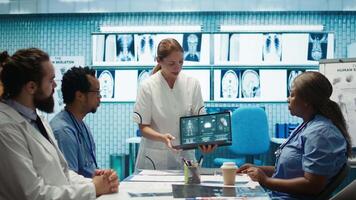 Diverse medical team examining test results and discussing innovative treatment plans at a modern clinic to enhance patient care quality. Doctors and nurses review x ray scans. Camera B. video