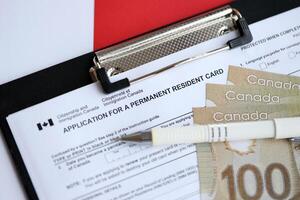 Application for permanent resident card on table with pen and canadian money photo