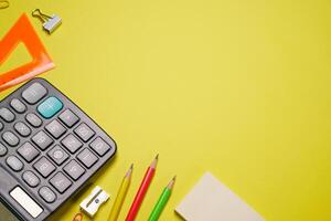 Calculator and stationery in different colors on a yellow background with copy photo