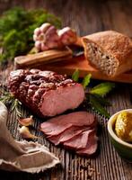 Sliced smoked ham on a wooden table with addition of fresh herbs and aromatic spices. Natural product from organic farm, produced by traditional methods photo