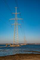 High-voltage power line against the background of the blue sky above the water of the lake photo