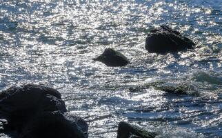 Bright reflections on the water on a sunny day among the coastal rocks near the Black Sea coast photo