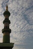 White and green mosque tower. Mosque tower with clouds in Indonesia background. photo