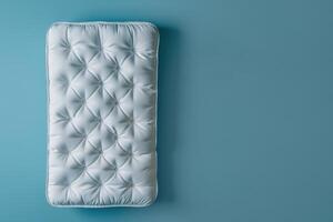 A cozy, tufted mattress resting against a serene blue wall in a minimalist bedroom setting photo