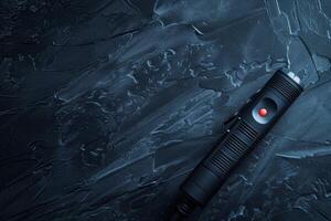 A sleek black laser pointer resting on a textured dark surface, illuminated by a soft light during a quiet evening photo