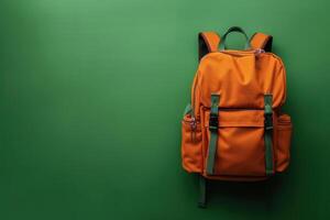 An orange backpack stands against a vibrant green background, showcasing its stylish design and functional features photo